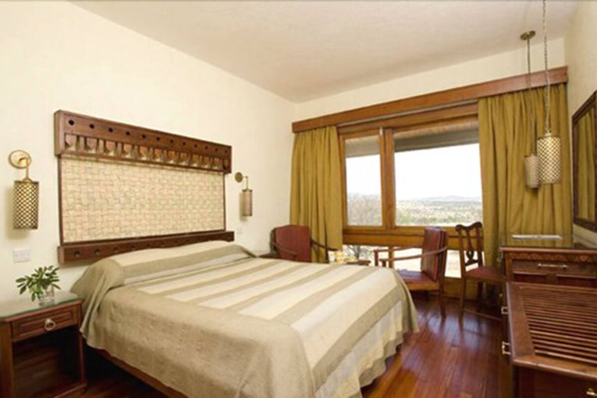 A hotel room with a large bed, a desk, a chair, a window with curtains, and a view of the city.