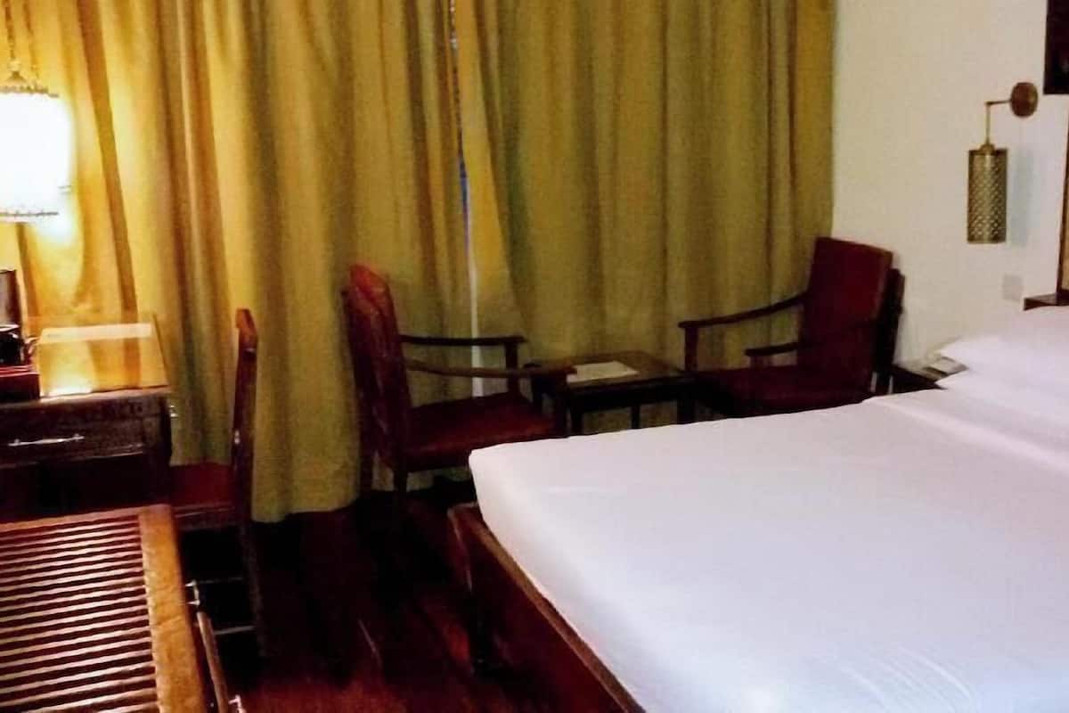 A hotel room with a bed, two chairs, a desk, and a lamp.