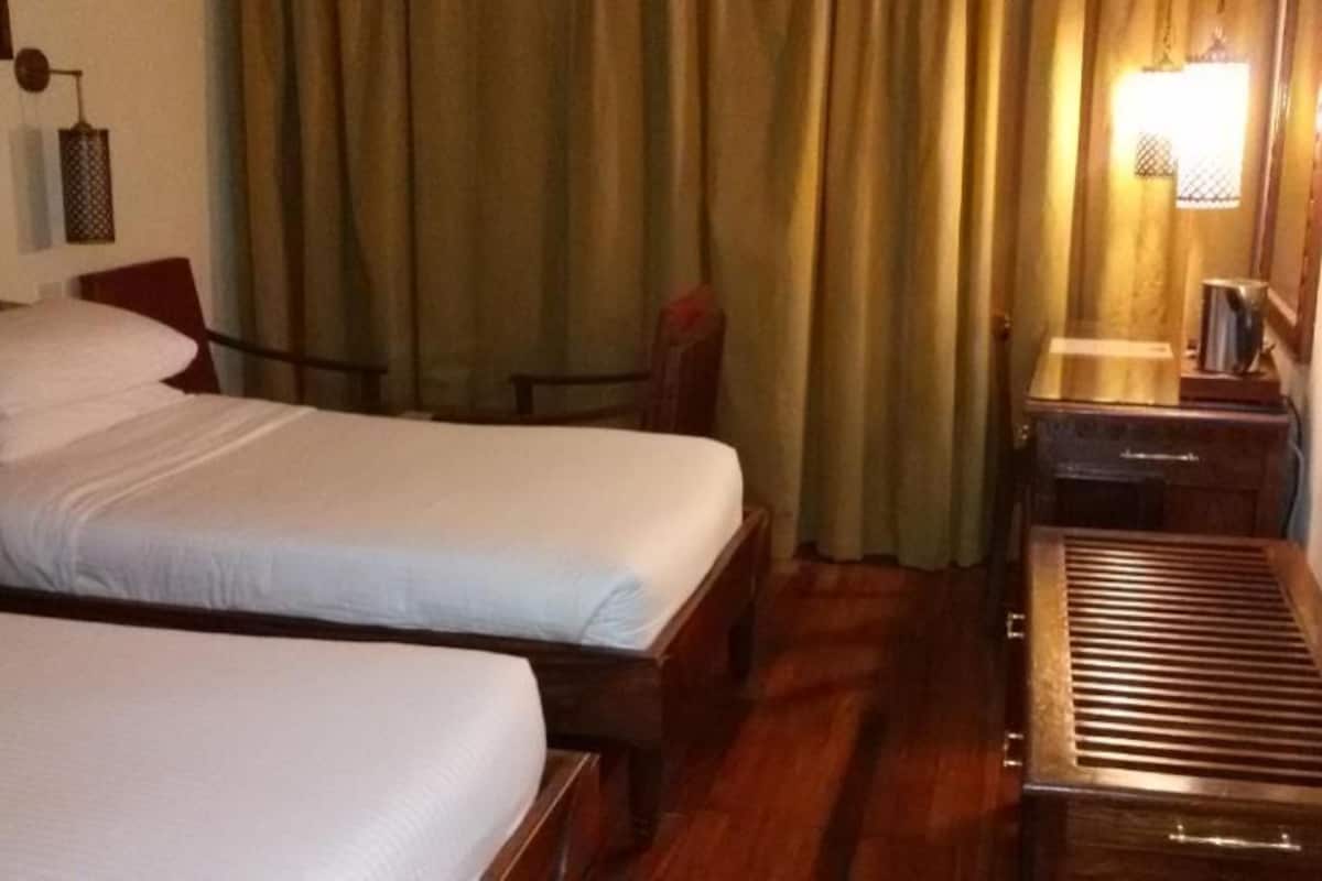 A hotel room with two beds, a wooden bench, a nightstand, and a lamp.