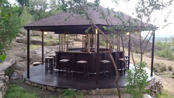 Un pabellón con base de piedra y cubierta de madera, que incluye una zona de bar con taburetes y un espacio para sentarse.