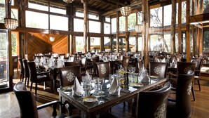Un comedor amplio con vigas de madera, ventanas grandes y sillones de cuero. Las mesas están preparadas con servilletas blancas y cubiertos.