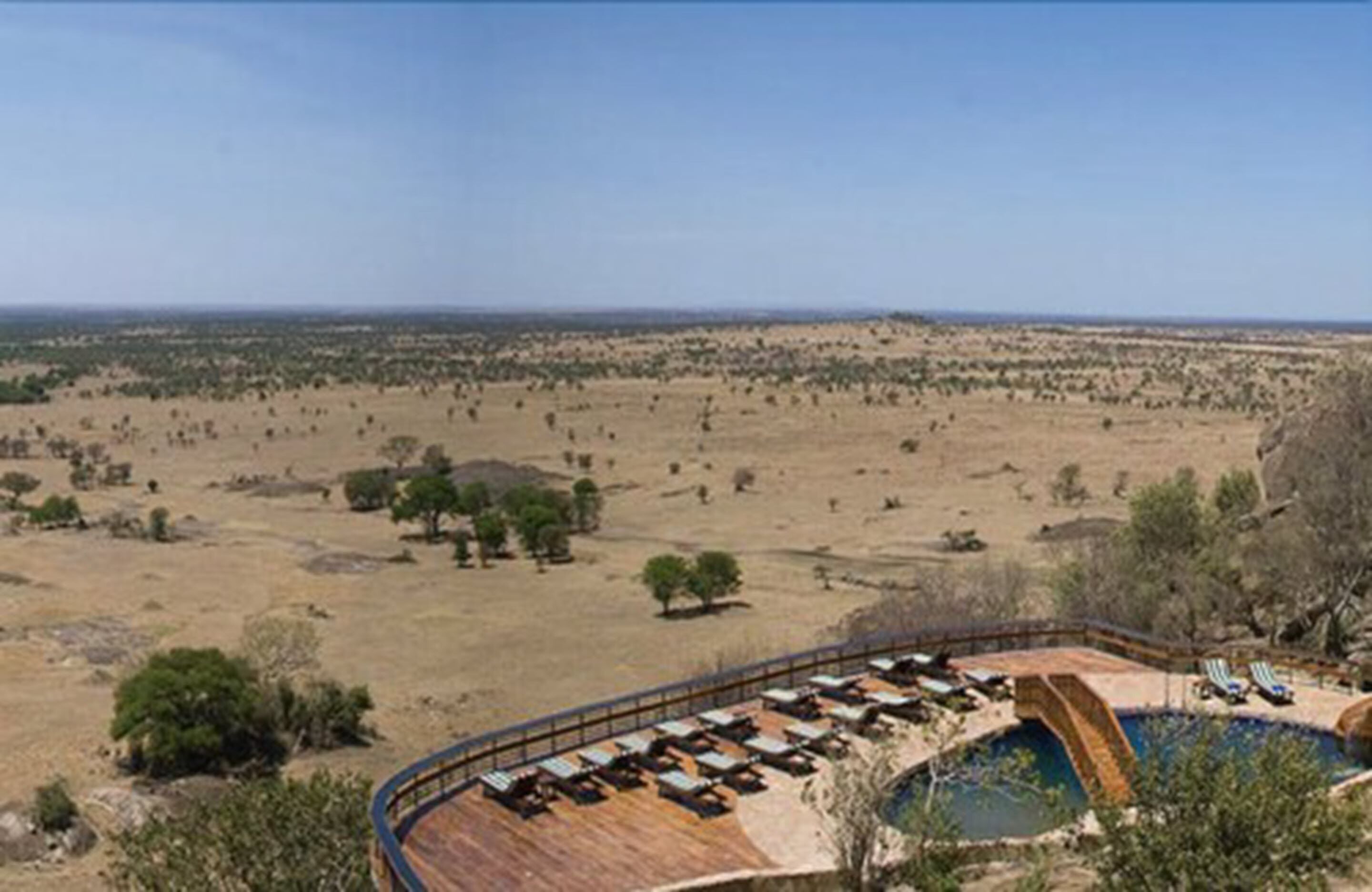 Un hotel con piscina y sillones de descanso, rodeado de un paisaje desértico.