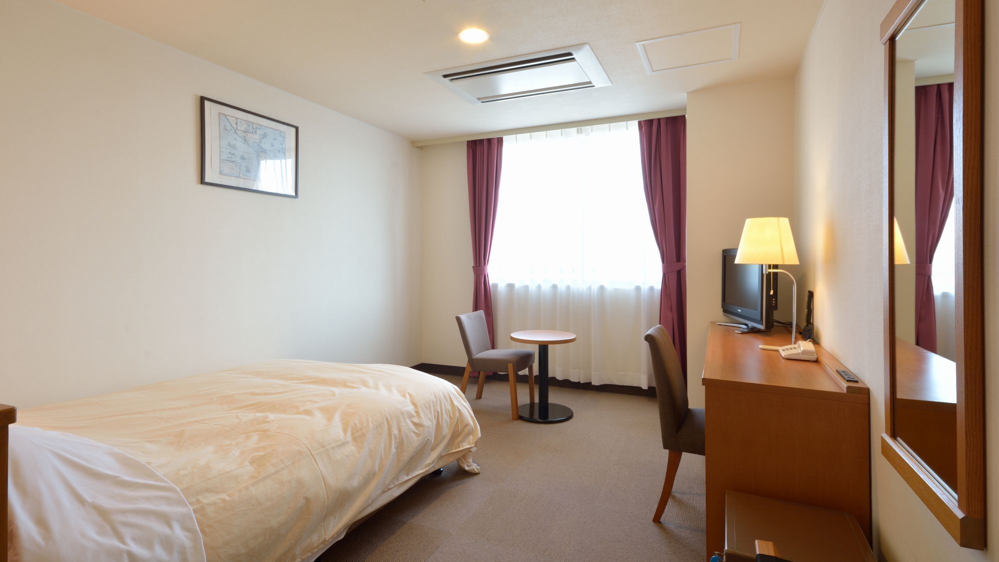 Habitación de hotel con cama, escritorio con lámpara, silla, televisor y ventana con cortinas.