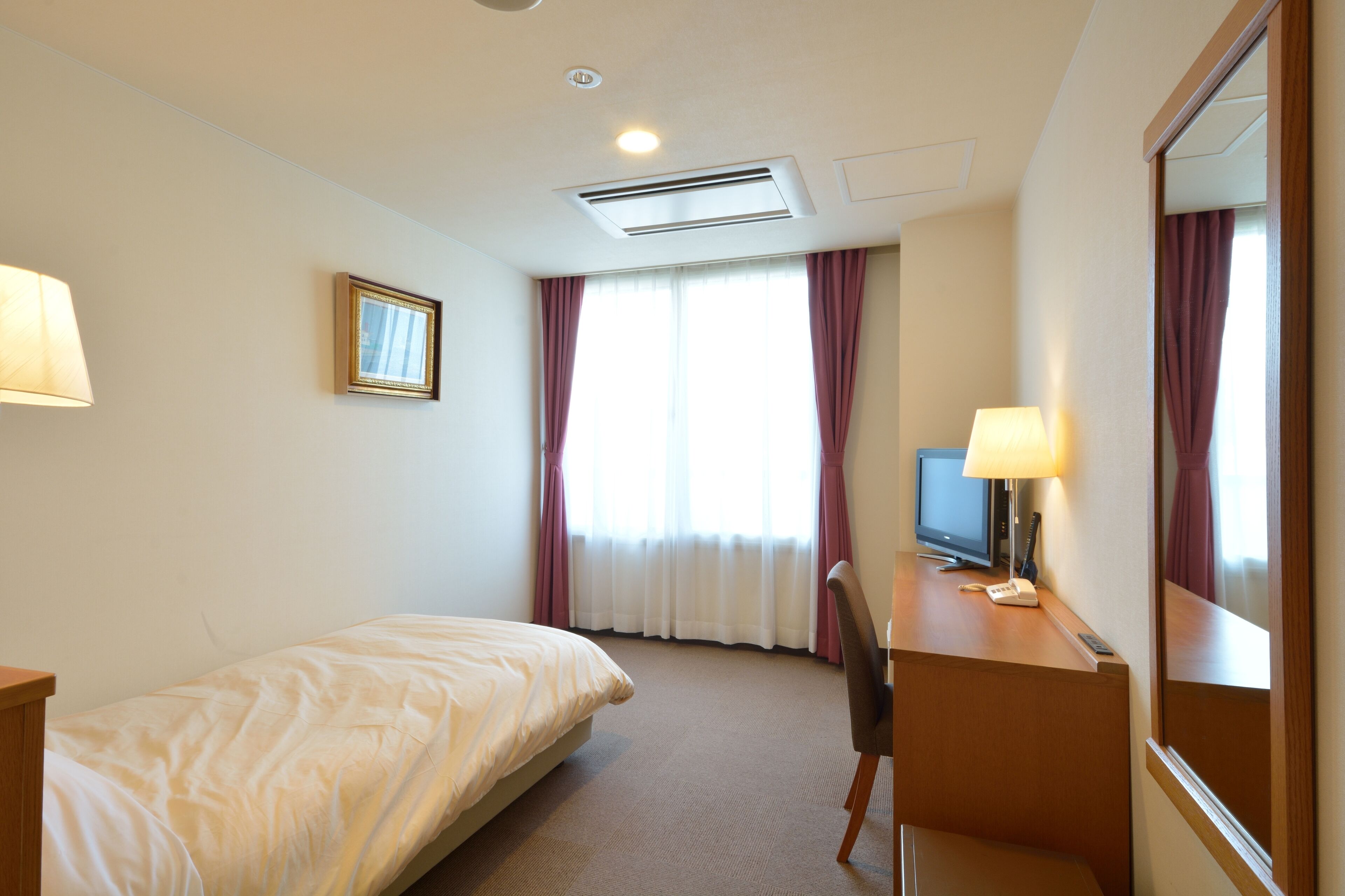 Una habitación de hotel con una cama, un escritorio con lámpara, un televisor y un espejo grande.
