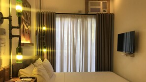 Ein Hotelzimmer mit einem Bett, einem an der Wand montierten Fernseher, einer Heizung und einem Fenster mit Vorhängen.