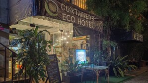La façade de l’hôtel Containers Eco, avec une enseigne pour le Bahay Kafe, est agrémentée de plantes en pot et dispose d’un espace de détente extérieur.