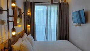 Une chambre d’hôtel avec un lit, un téléviseur fixé au mur, une fenêtre avec des rideaux et un climatiseur mural.