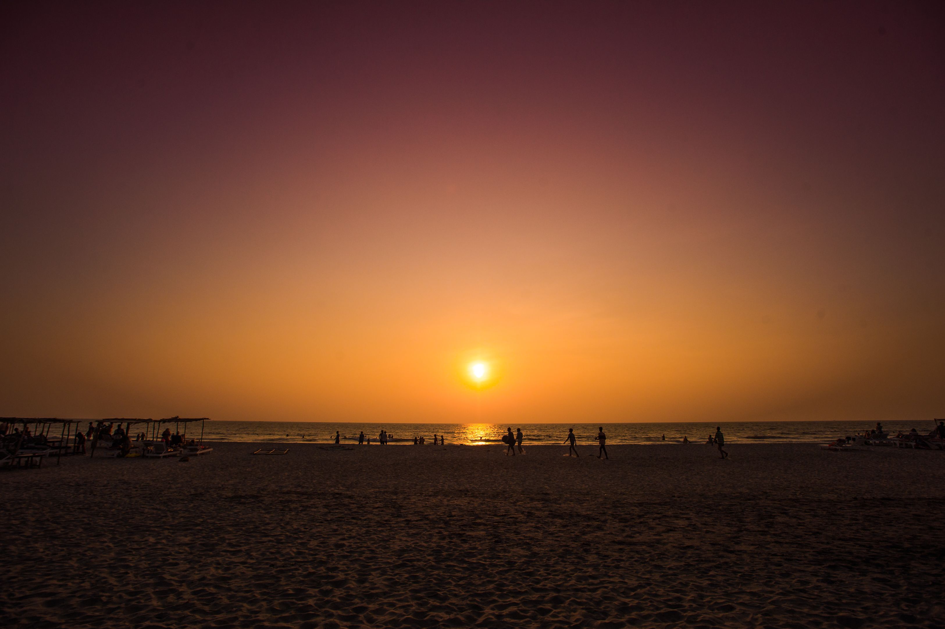 A beach at sunset with people walking and sitting on the sand.