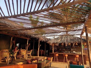 Zona de bar al aire libre con estructuras de bambú, mobiliario de mimbre y una barra.