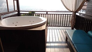 Un balcon avec une grande baignoire, une terrasse en bois et un canapé bleu.