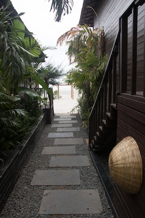 A pathway leading to a wooden building with a thatched roof, surrounded by tropical plants.