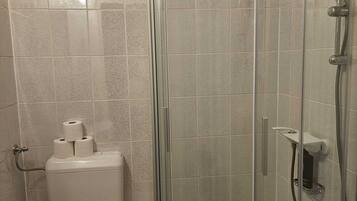 Un baño con inodoro, ducha con mampara de vidrio y pared de azulejos.