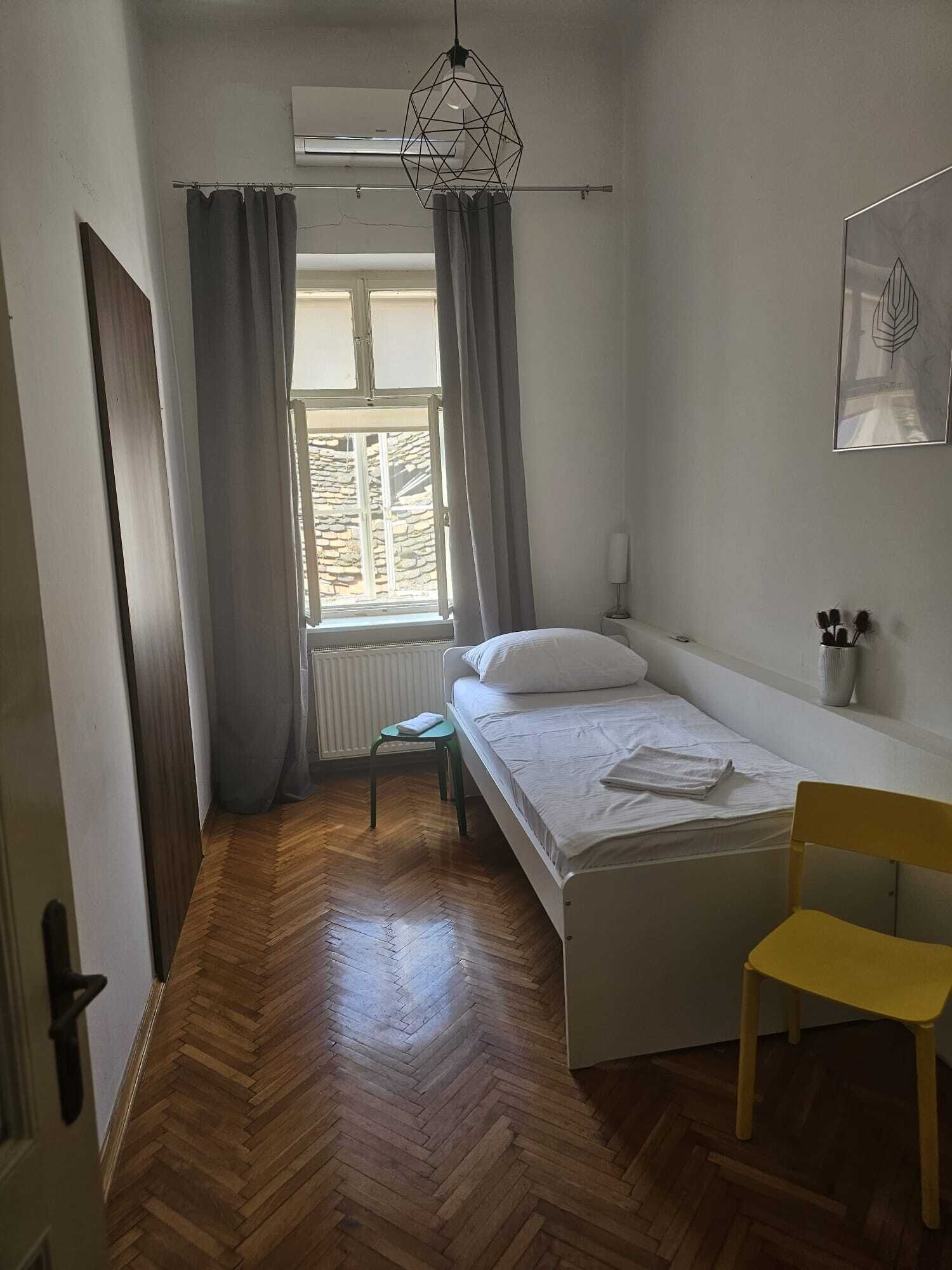 A small, clean room with a bed, a chair, a window, and a radiator.