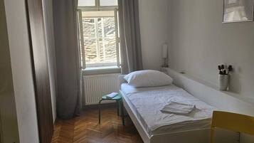 A small, clean room with a bed, a chair, a window, and a radiator.
