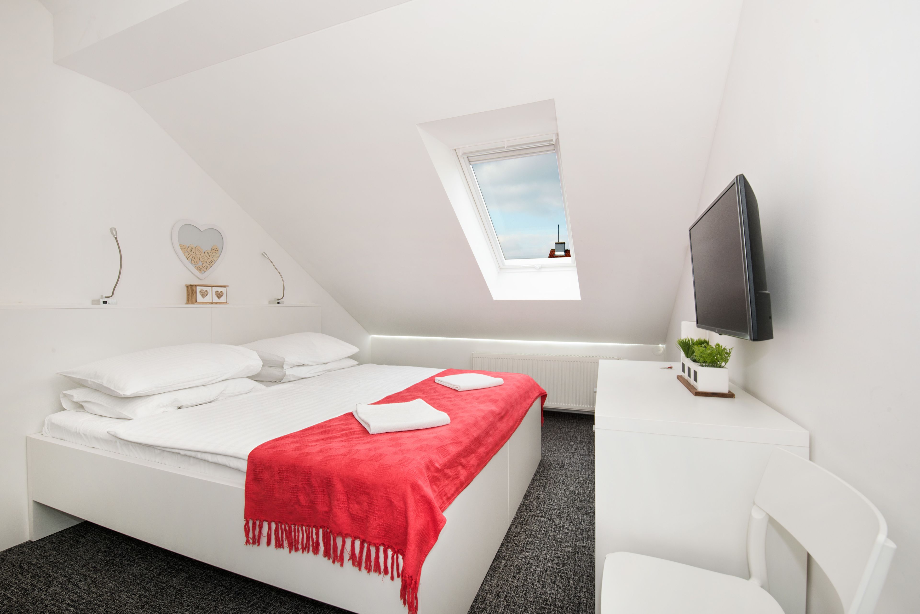 Een moderne slaapkamer met een bed, een bureau, een televisie en een dakraam.
