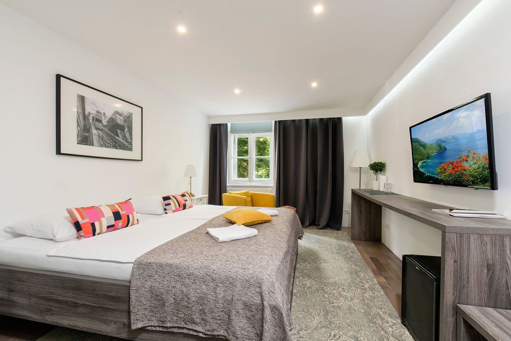 Habitació d'hotel moderna amb un llit gran, escriptori, televisió i finestra amb cortines.