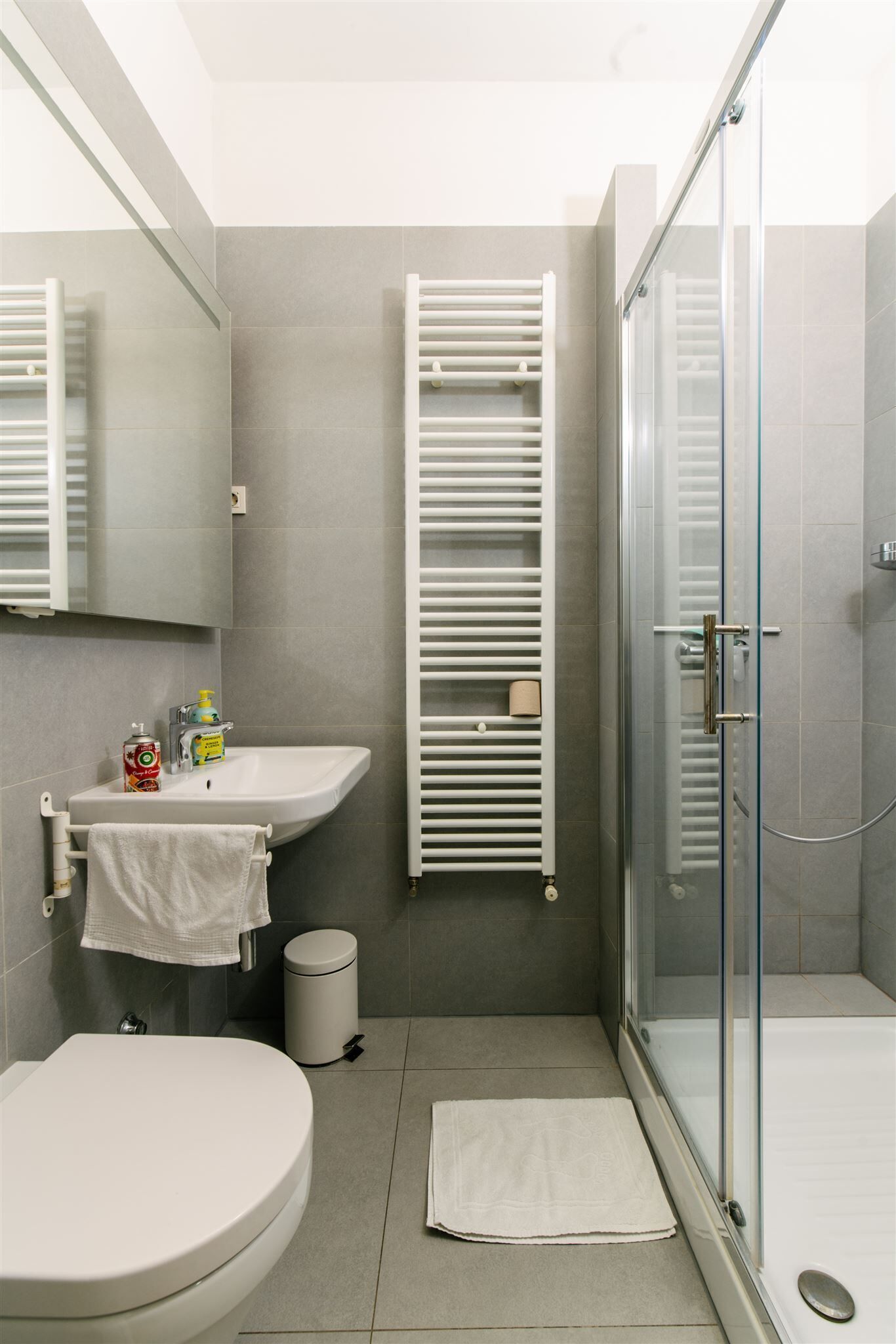 A modern bathroom with a toilet, sink, glass shower enclosure, and a towel rack.