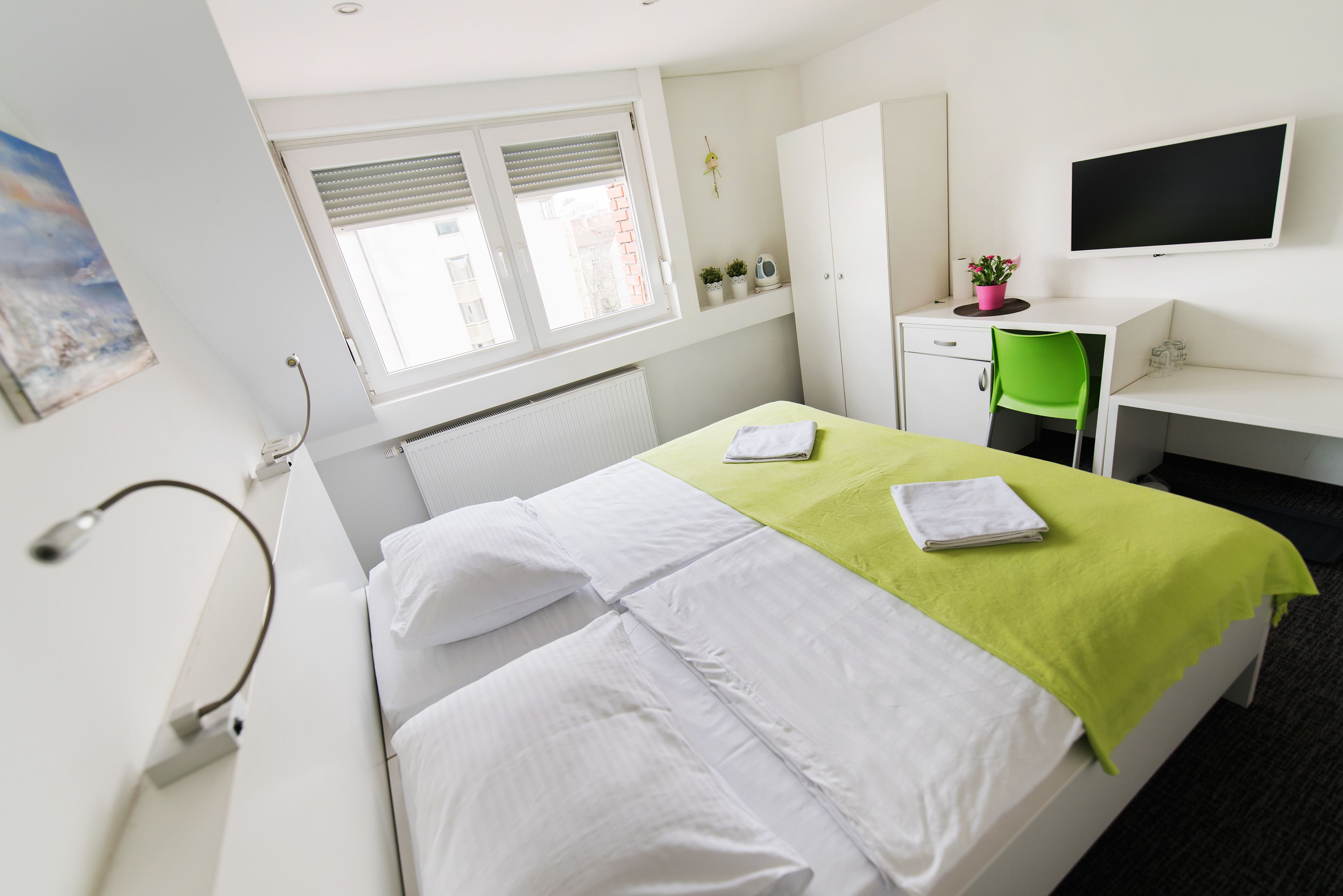 A hotel room with a bed, a desk, a chair, a TV, and a window with blinds.