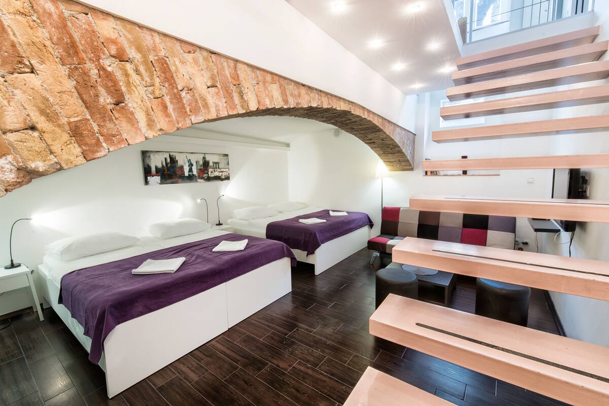 Ein modernes Hotelzimmer mit zwei Betten, einer Decke aus Steinbogen, einer Treppe und Blick auf die Stadt.