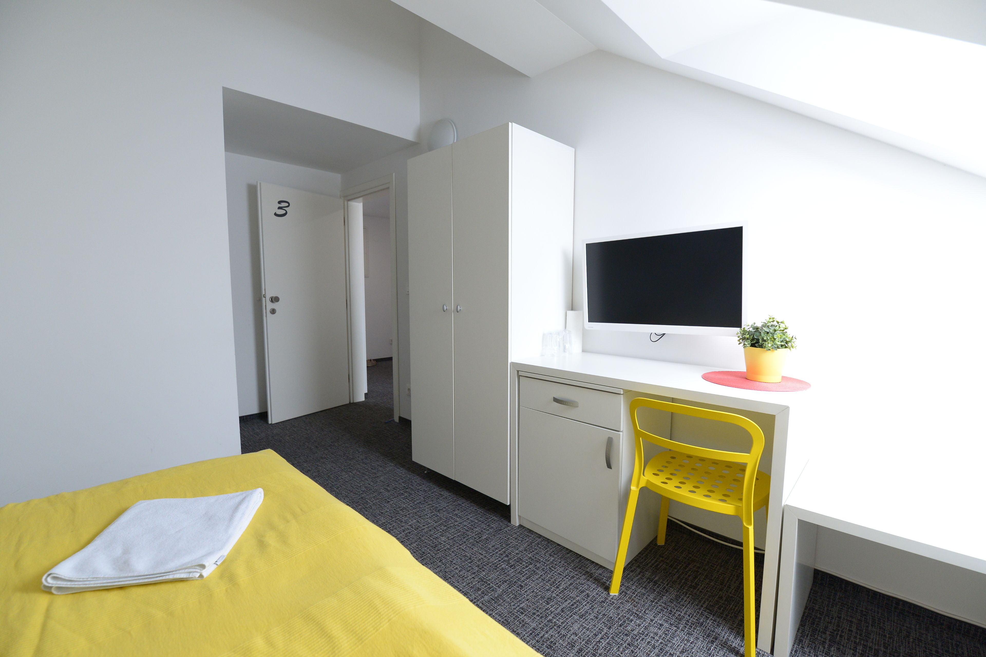 Una habitación con una cama, un escritorio con una silla, un televisor y una puerta.