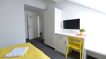 Una habitación con una cama, un escritorio con una silla, un televisor y una puerta.