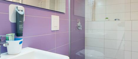 A modern bathroom with a white sink, purple walls, and a glass-enclosed shower area.