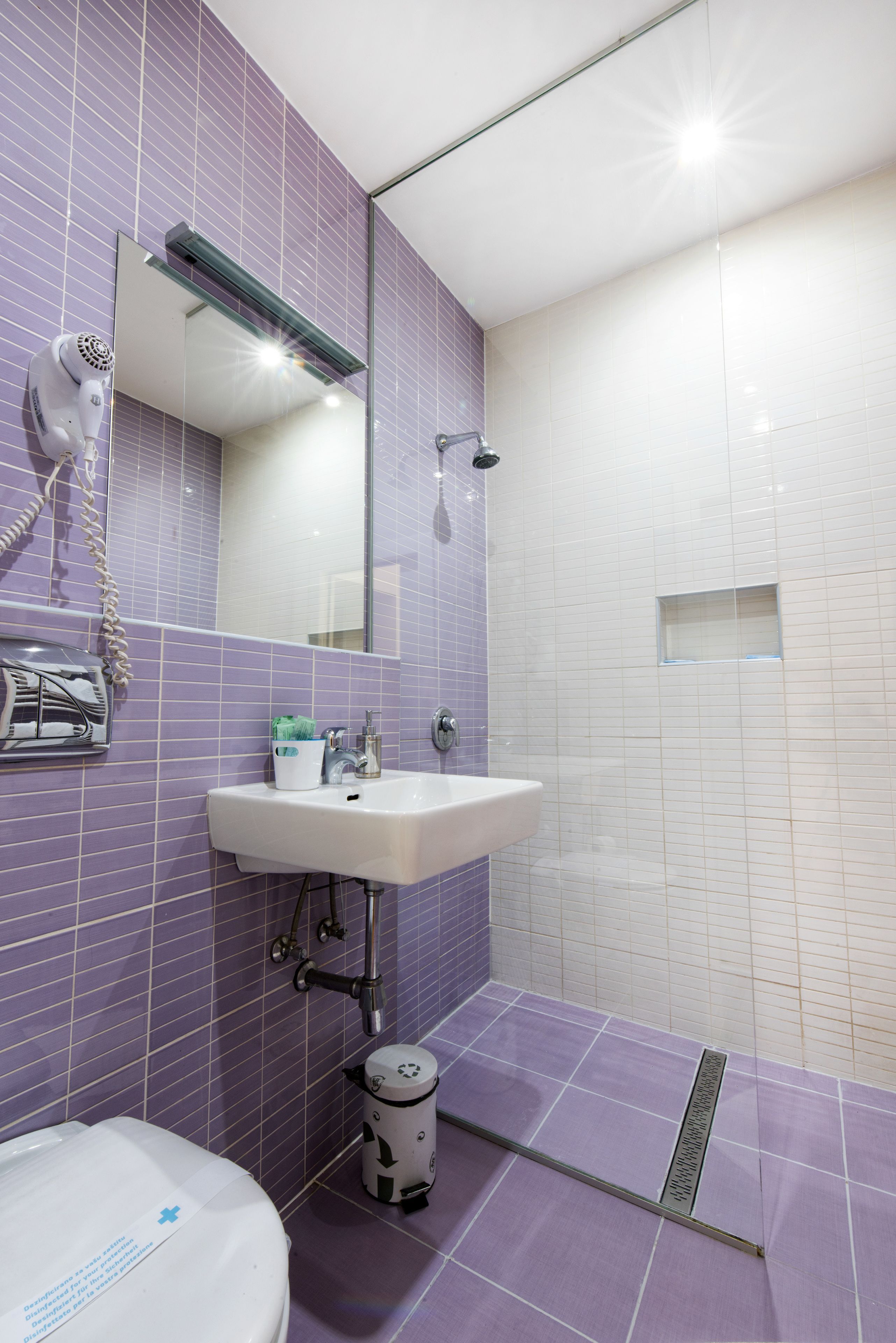 Un bagno con piastrelle viola, un lavandino bianco, uno specchio, un asciugacapelli e una doccia.
