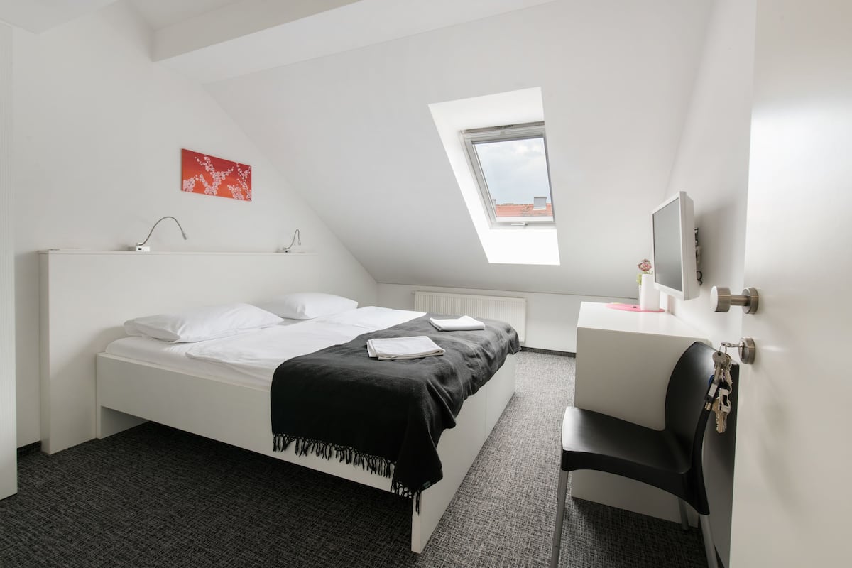 Ein modernes Hotelzimmer mit Bett, Schreibtisch, Stuhl, Fernseher und einem Oberlicht.