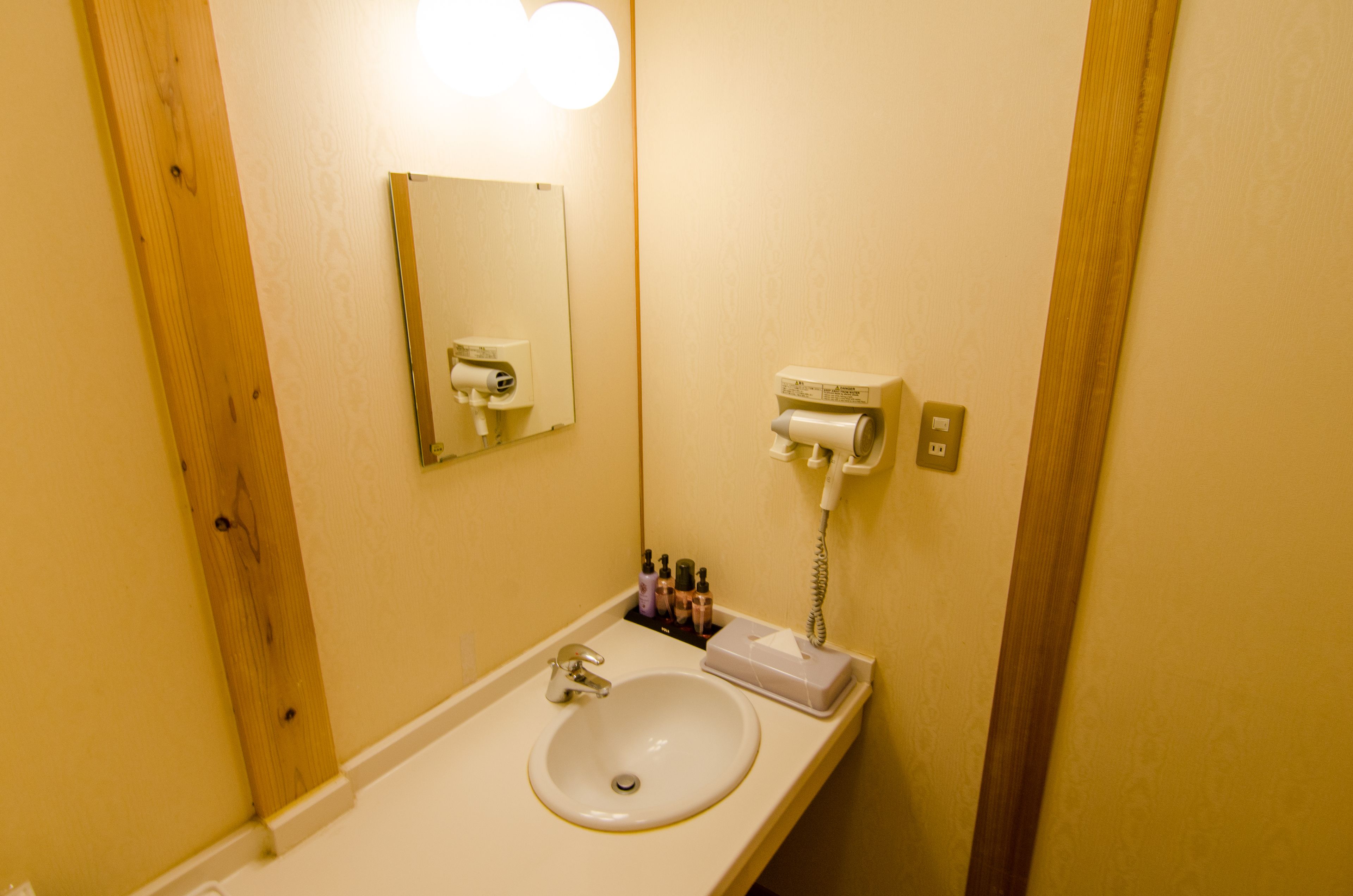 Un baño con lavabo blanco, espejo, secador de pelo y teléfono.
