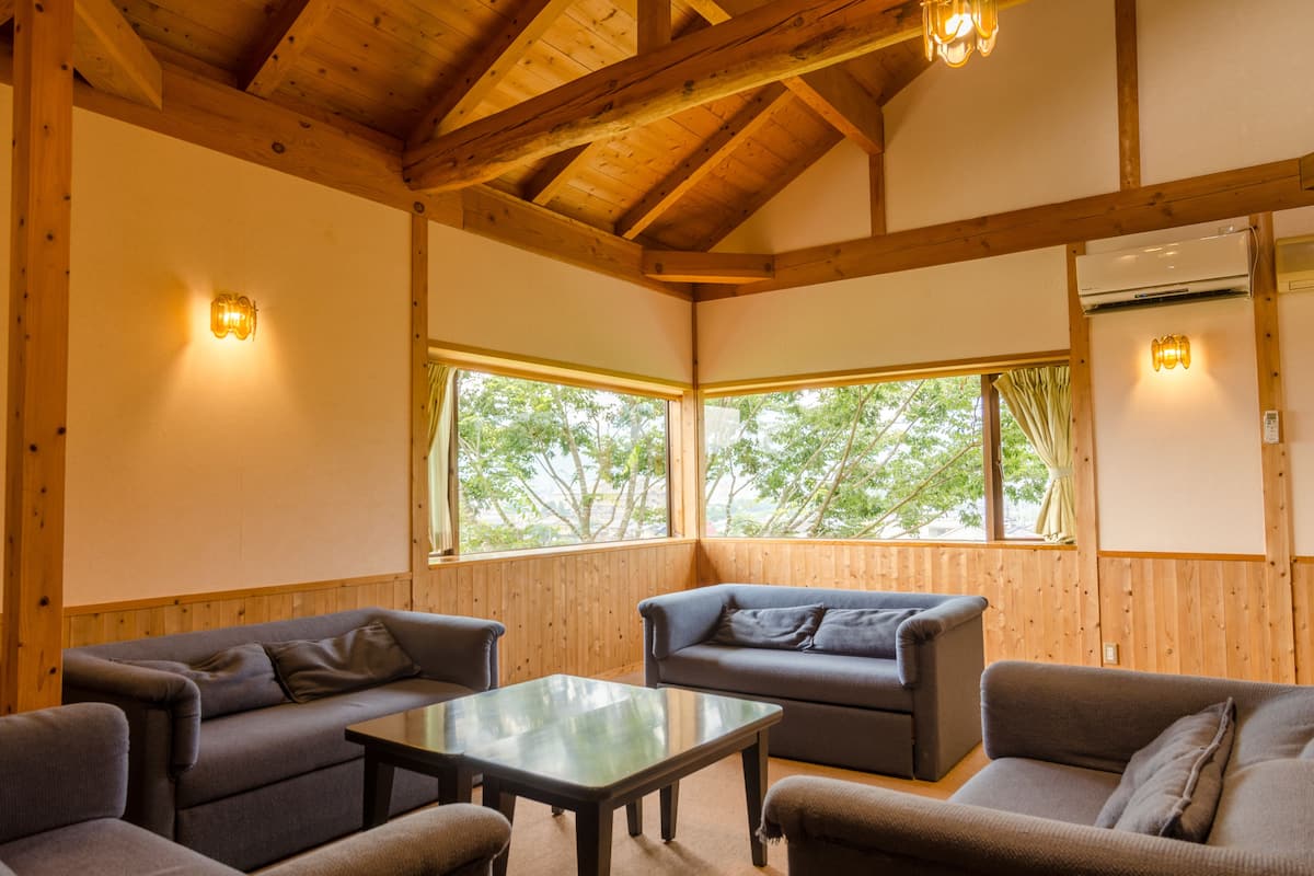 A cozy room with wooden beams, a sofa, a table, and large windows with curtains.