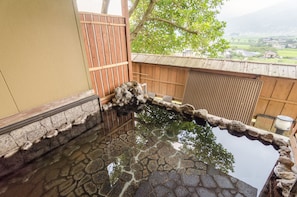 A traditional Japanese garden with a stone pond, wooden fence, and a view of the countryside. - Ryokan Fukinoya (Yufu)