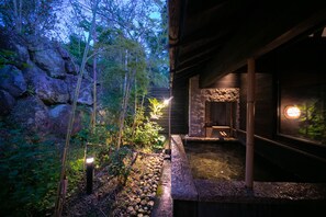 A serene garden with a stone pathway, bamboo, and a small water feature, leading to a wooden building with a stone wall and a glass door. - Ryokan Fukinoya (Yufu)
