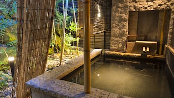 A traditional Japanese onsen with stone steps leading into a hot spring, surrounded by bamboo and greenery.