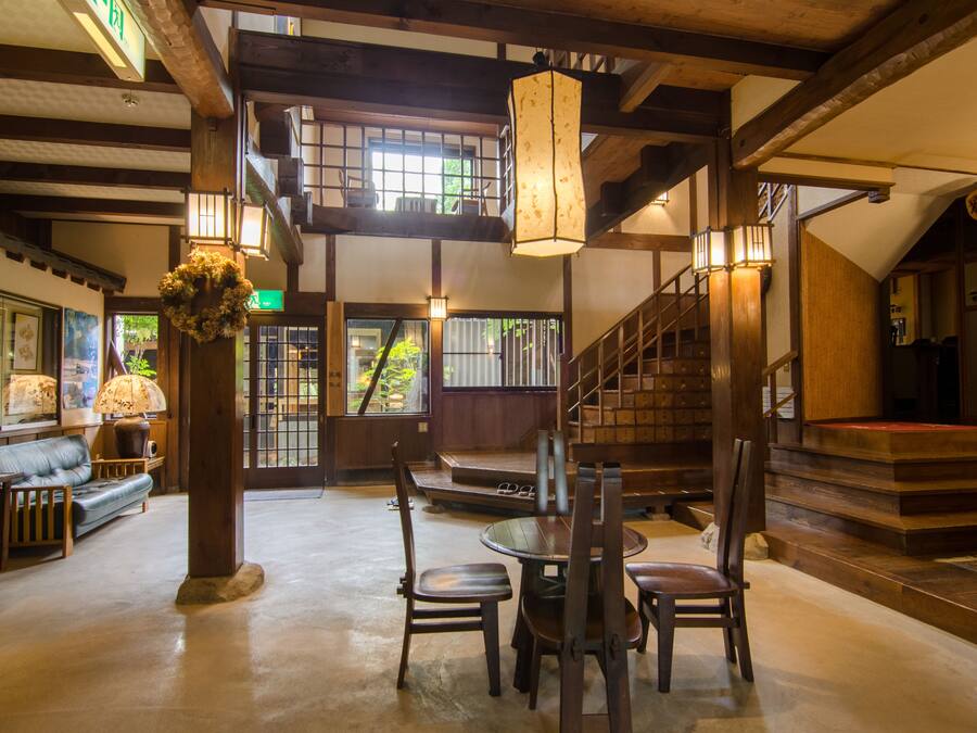 A traditional Japanese inn with tatami mat flooring, a wooden staircase, and a reception area with a sofa and chairs.