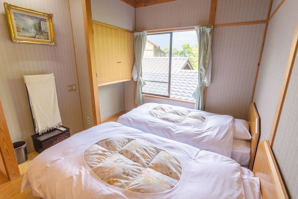 A room with two beds, a window with curtains, a wooden cabinet, and a framed picture on the wall.