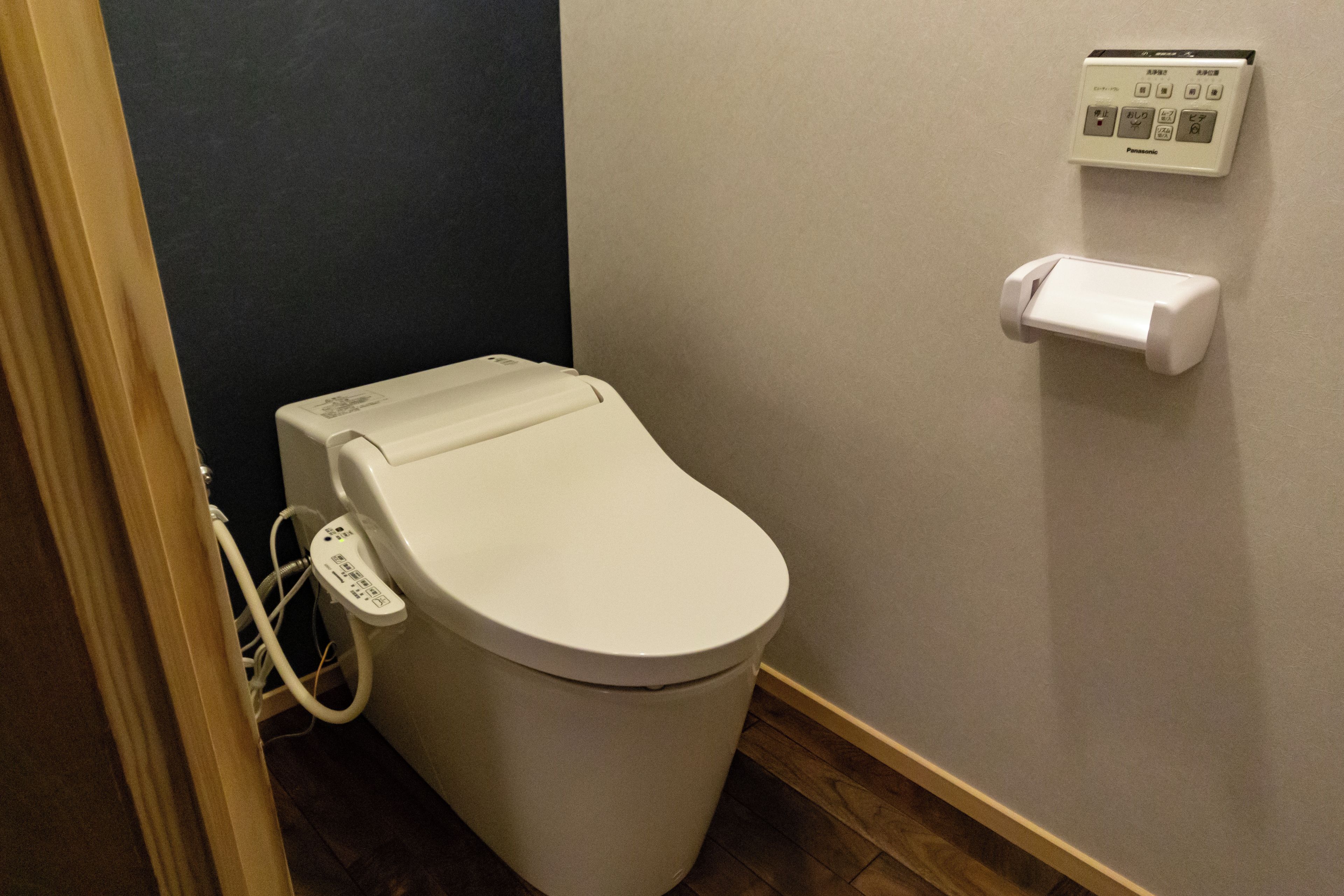 A white toilet with a control panel and a toilet paper holder on the wall.