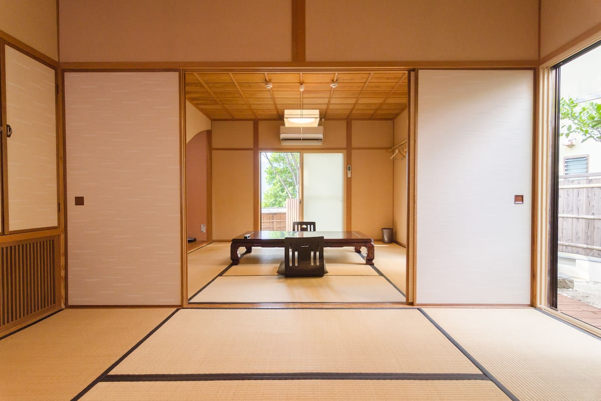A traditional Japanese room with tatami flooring, a sliding door, and a table with chairs.