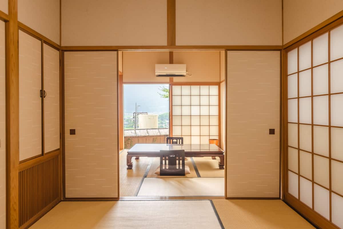 A traditional Japanese room with tatami flooring, shoji screens, and a sliding door leading to a view of the outside.