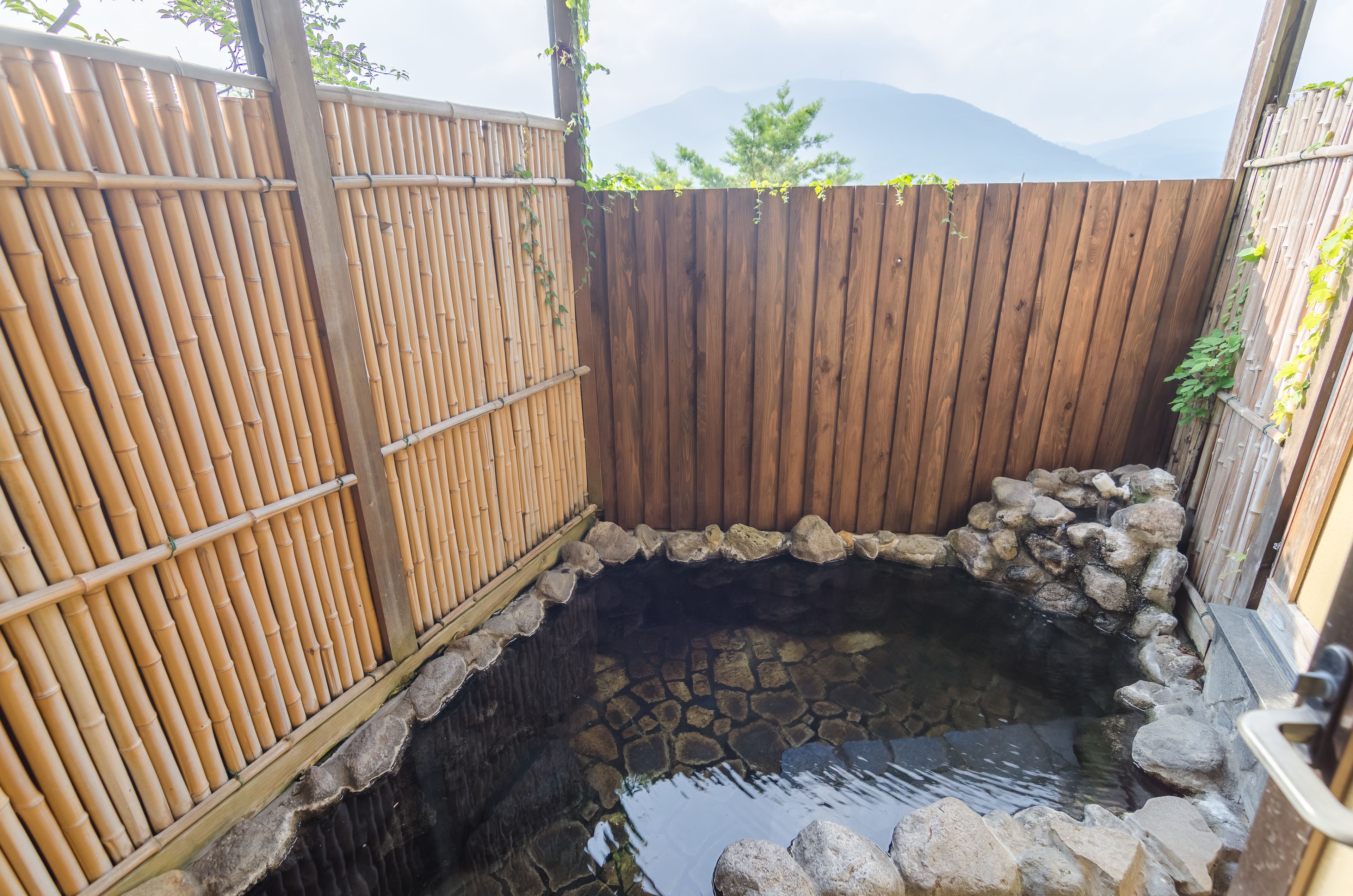 A traditional Japanese onsen with a wooden fence and stone basin.