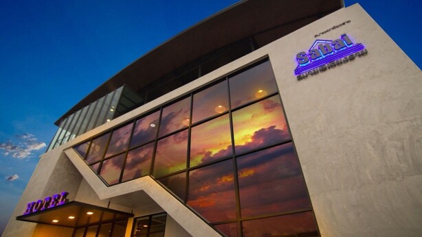 A hotel with a modern architectural design, featuring a prominent glass facade reflecting a sunset. - Sabai@Chiang Rai (Chiang Rai)