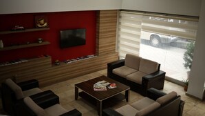 A modern living room with a red accent wall, a flat-screen TV, and a large window with blinds. - Otel Altay (Samsun)