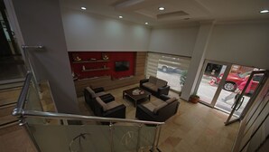 A modern interior with a staircase, a seating area with sofas and a coffee table, a TV mounted on a red wall, and a view of a red car outside through a glass door. - Otel Altay (Samsun)