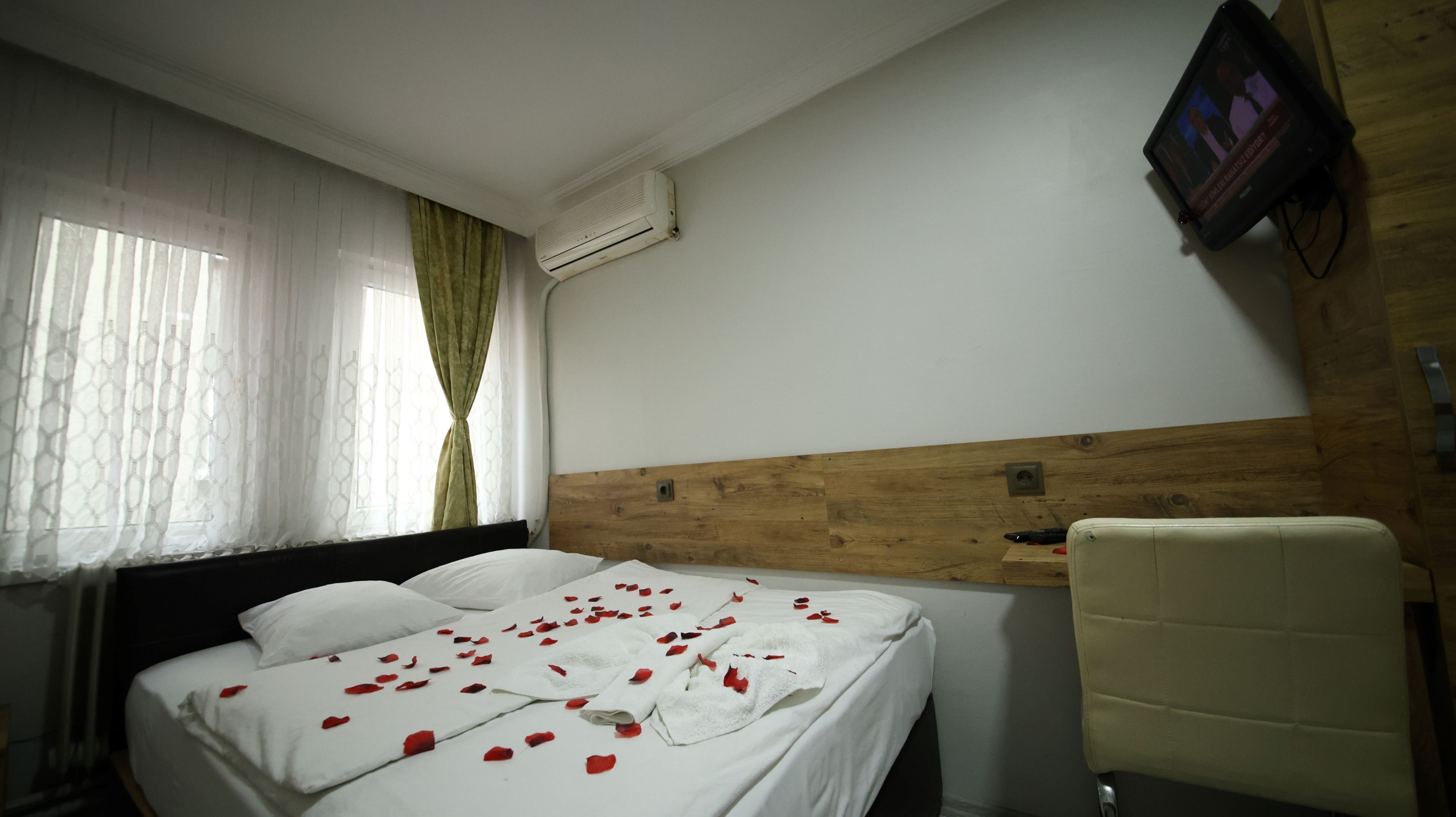 Quarto de hotel com cama, cabeceira de madeira, televisão presa na parede e uma cadeira.