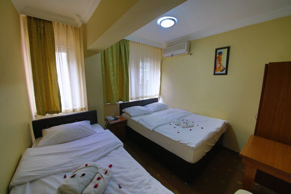 Una habitación de hotel con dos camas, una mesita de noche con teléfono, una mesita auxiliar de madera y un equipo de aire acondicionado en la pared.