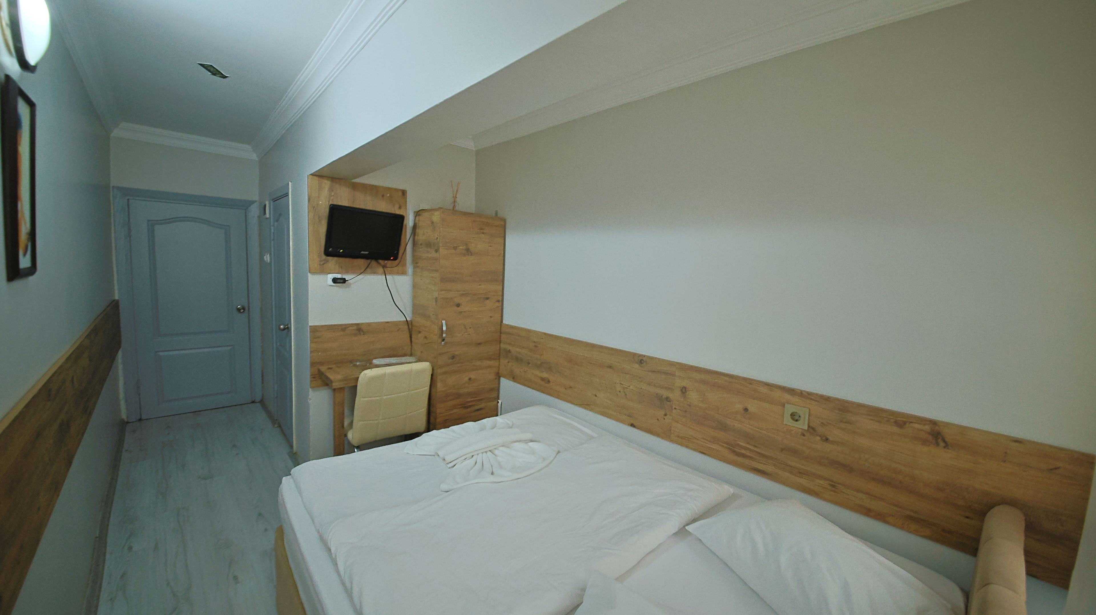 A bedroom with a wooden headboard, a bed with white bedding, a small bedside table, and a mounted TV.
