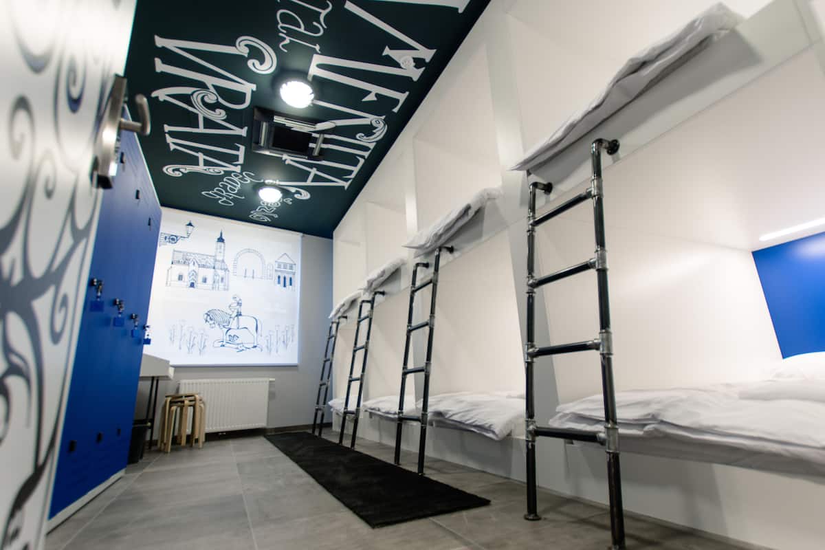 Ein Zimmer mit Etagenbetten, Leitern, einem schwarzen Teppich und einer Projektion eines Gebäudes an der Wand.