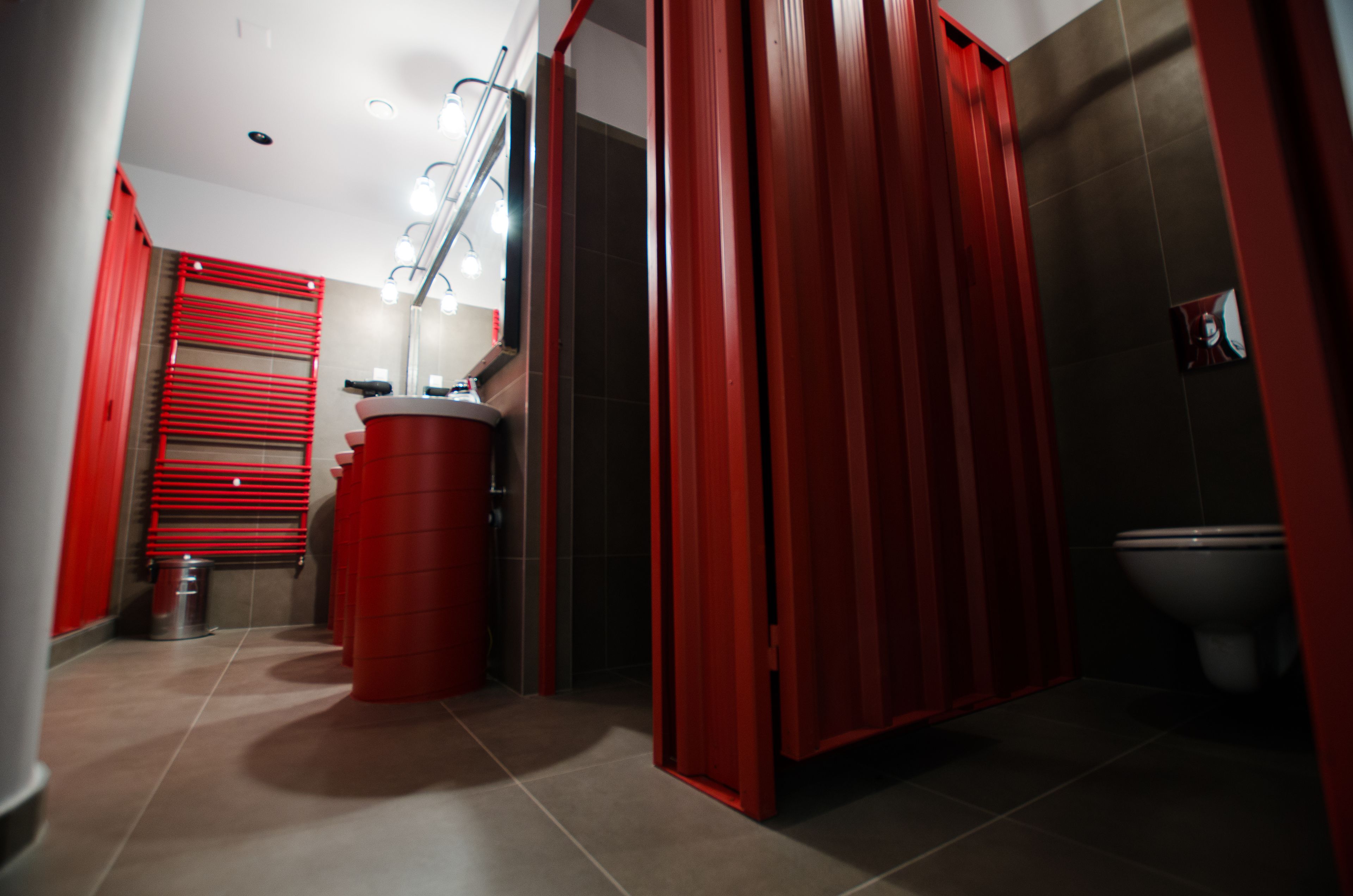 Un bagno con box doccia rosso, un water e un lavandino con uno specchio sopra.
