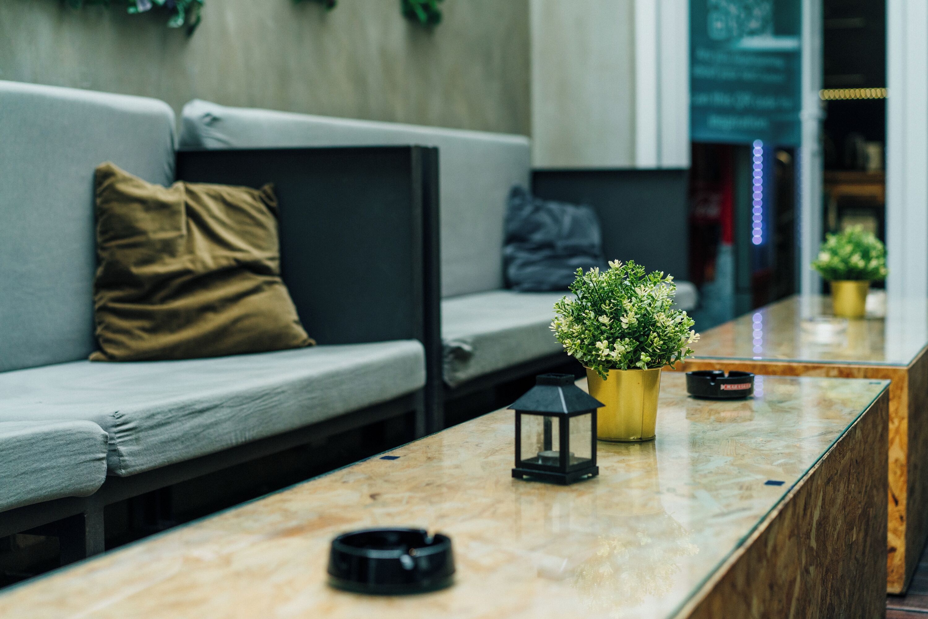 Uma área de recepção moderna com balcão de mármore, sofá com almofadas, uma pequena planta em vaso e um candeeiro preto.