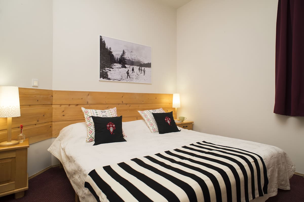 Une chambre d’hôtel avec une tête de lit en bois, un grand lit avec une literie à rayures noires et blanches, deux lampes de chevet et un tableau encadré au mur.