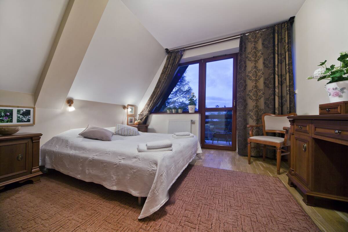 Une chambre à coucher comprenant un lit, une commode, une chaise, une fenêtre avec des rideaux et un radiateur.